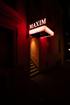 暗闇の中に赤く鮮やかに光る「MAXIM」のネオン看板と、奥へと続く階段の入り口
