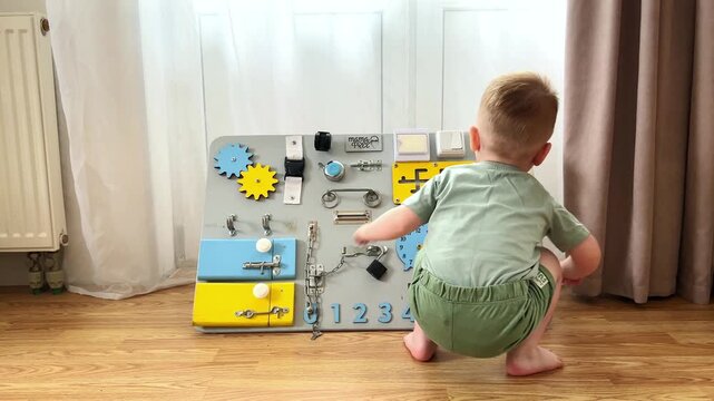 Child playing with zippers, switches and wheels on busyboard. Small hand movements strengthen muscles. Early education through sensory play. Discovering physical world