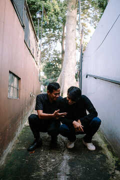 Two Men Squatting in a Narrow Alleyway Talking