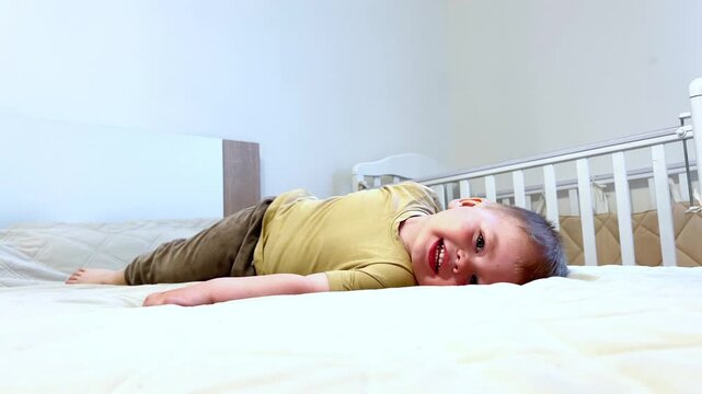 Caucasioan baby in playful pose, playing on soft white bed, happy smile, chubby cheeks. Pure joy and playful spirit