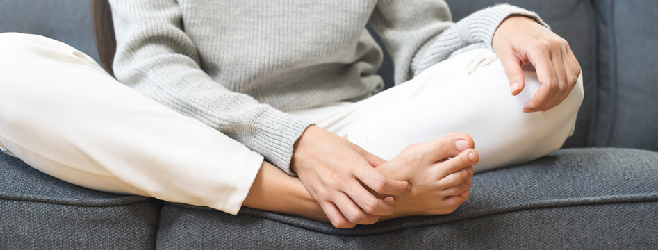Foot pain, Smelly feet woman hand scratch feet, itch foot, problem itchy skin sitting on sofa at home, dermatitis from fungus, fungal bacterial infection, allergic reaction, eczema. Foot care concept.