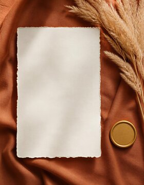 Luxury autumn terracotta wedding invitation card mockup with blank copy space on terracotta linen fabric. Flat lay with deckled edge ivory paper, gold wax seal, pampas grass, and leaf gobo shadows in 