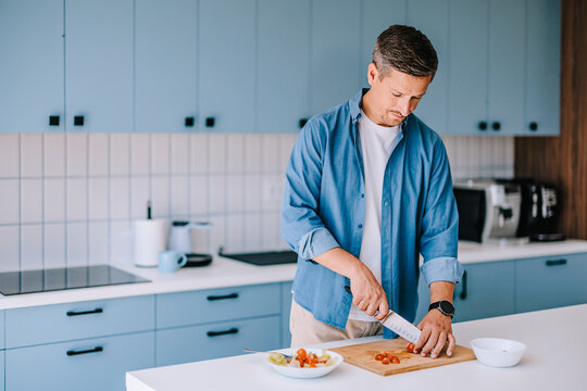Man Chopping Tomatoes in Modern Home Kitchen Preparing Healthy Meal While Focused and Casual