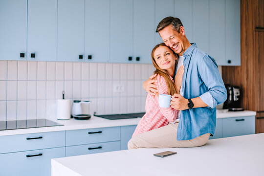 Happy Couple Hugging in Modern Home Kitchen Holding Coffee Mug, Casual Morning Together