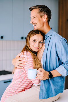 Loving Couple Hugging in Kitchen While Sharing Morning Coffee &mdash; Casual Home Romance
