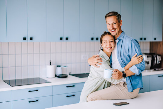 Smiling Couple Hugging in Modern Kitchen While Sharing Morning Coffee and Cozy Home Moments