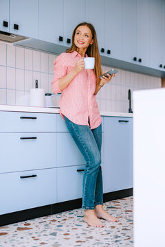 Relaxed Woman Drinking Coffee in Bright Kitchen While Checking Smartphone &mdash; Morning At-Home Moment