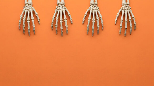 Four human skeleton hands arranged in a row on a vibrant orange background for Halloween.