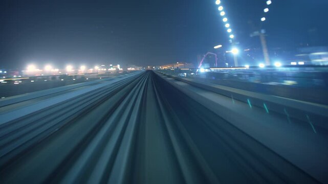 Front POV rushes forward along an elevated transit railway track at night, passing illuminated construction lights toward distant buildings