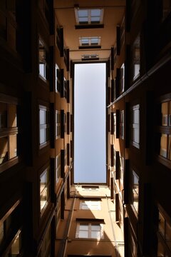 Looking up view of sky from bottom of narrow courtyard well, surrounded by old building walls and windows
