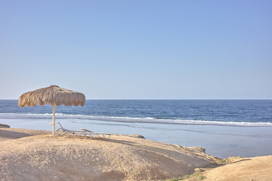Straw beach umbrella and lounge chairs on a beautiful sandy beach.