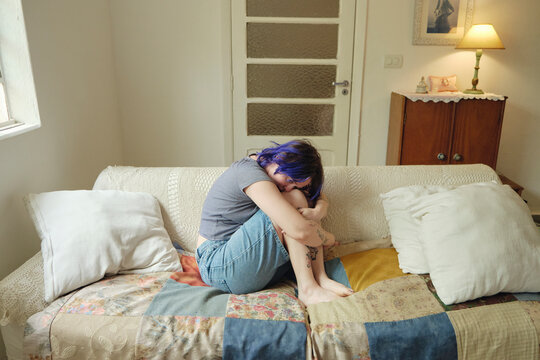 Young non-binary person curled up on a patchwork sofa