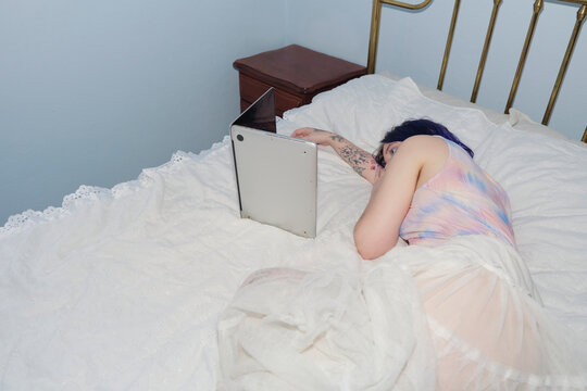 Non-binary person lying in bed watching something in their laptop