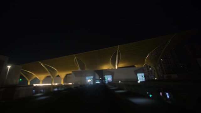 Front train POV glides into an illuminated station at night, passing an oncoming passenger train on adjacent tracks before continuing into the dark