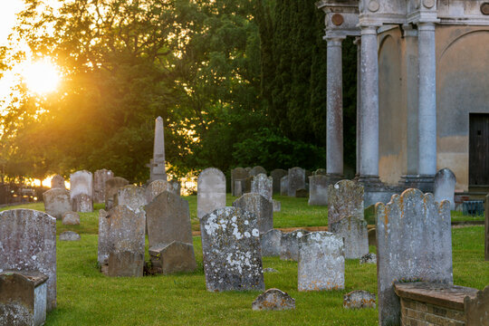 Historic graveyard in Mistley, England, bathed in warm sunset light, with weathered gravestones, lush grass, and distinctive church architecture. Ideal for heritage and travel themes.