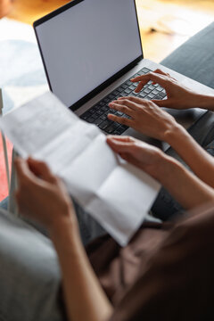 Partial view of women checking financial papers with laptop on sofa