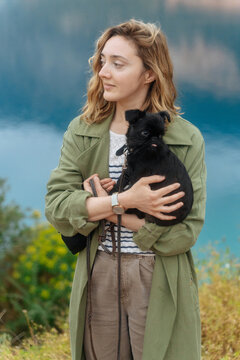 Woman holding small black dog near lake