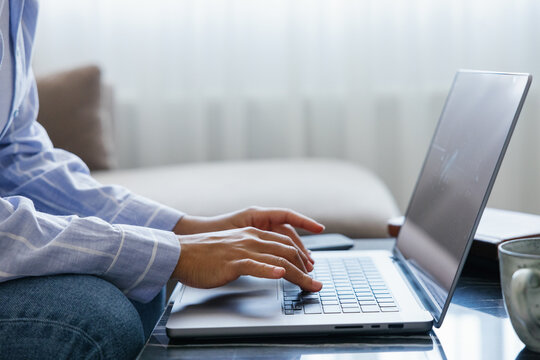 Partial black woman typing laptop computer at desk at blurred home