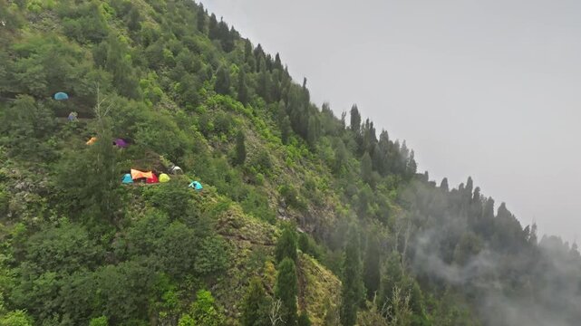 Agung mountain slope on Bali island. Multiple colorful tents set up on the lush green forest hill, remote camping trekking experience, dense forest and low-hanging clouds. Trekking and active sports