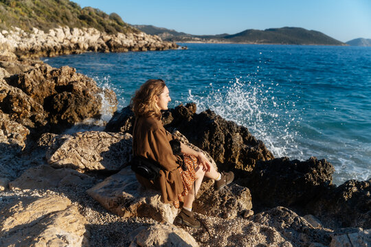 Woman sitting on rocky shore by the sea