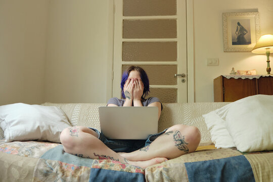 Non-binary person working in their laptop covering their face