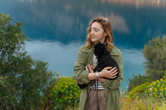Woman holding dog near blue lake