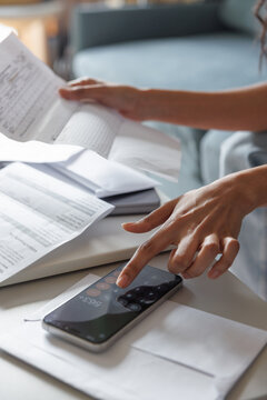 Partial woman checking financial documents at desk at blurred home