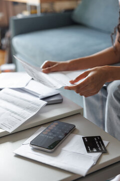 Cropped woman checking financial documents at desk on sofa