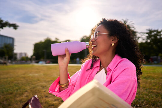 Young woman enjoying refreshing drink in park sunshine