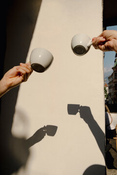 Hands holding coffee cups with shadows on sunny cafe wall