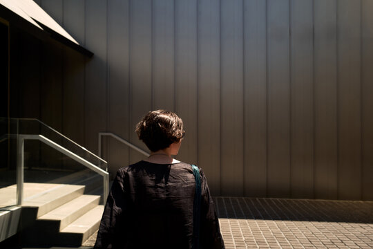 Woman Walks Towards Large Metal Wall in Urban Setting