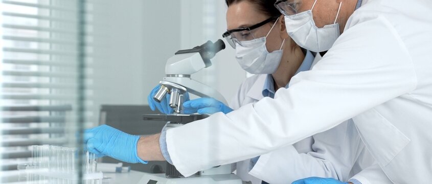 Medical researchers in protective masks. Safety glasses. And blue gloves are meticulously working with a microscope