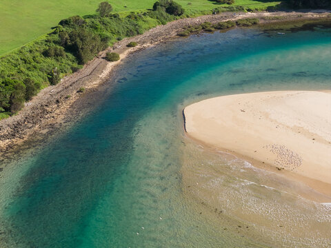 A coastal river rounding a sandy beach and flowing out to sea