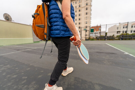 anonymous person holding pickleball paddles walking on court