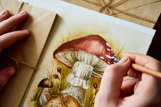 Artist hand painting white details on a watercolor mushroom