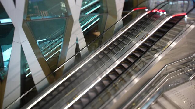 Empty modern escalators with glowing handrails run inside a futuristic glass building with geometric architecture