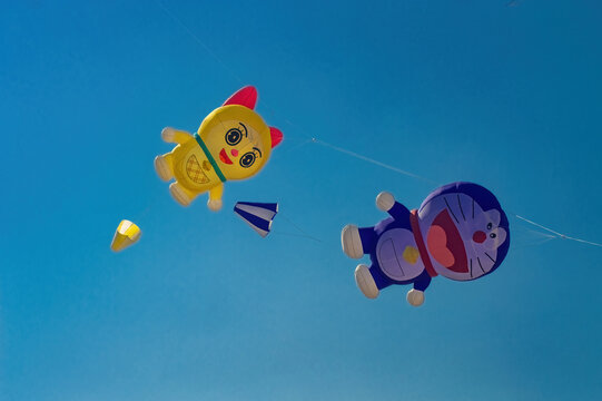 Surabaya, Indonesia - August 30, 2026: Colorful Doraemon and Dorami character giant kites flying high in clear blue sky during annual outdoor kite festival, Indonesia, 30 August 2026