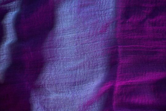 A piece of fabric lies on a surface as light catches its texture. The colors blend from purple to blue