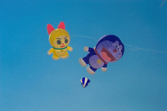 Surabaya, Indonesia - August 30, 2026: Doraemon and Dorami character shaped giant inflatable kites soaring high in the clear blue sky at Surabaya Kite Festival, Indonesia, 30 August 2026
