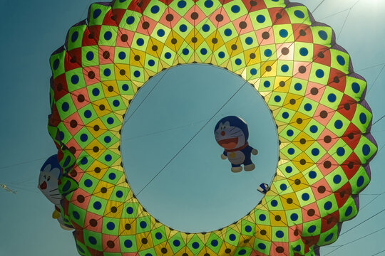 Surabaya, Indonesia - August 30, 2026: Colorful giant ring kite flying with a Doraemon character kite in the center during the annual outdoor kite festival, Indonesia, 30 August 2026