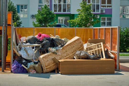 Spring mattress leaning against overfilled plastic trash bags at an unofficial waste collection site in a residential area