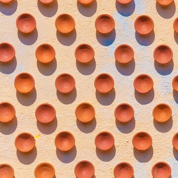 Diwali diya oil lamps arranged in a repetitive pattern on a cream plaster wall, featuring warm russet tones for festive greeting cards and banners