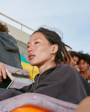 Young East Asian woman with locs and earphones sitting on stadium bleachers, a natural moment of quiet focus with copy space for music or fitness