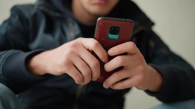 Close up of young man holding and interacting with red smartphone focusing on his hands gripping device. scene is indoors with soft lighting showing consistent engagement without significant