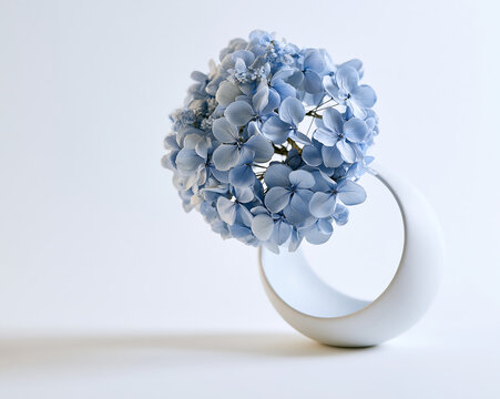A spherical arrangement of light blue hydrangea flowers placed inside a white circular ceramic vase on a clean white background