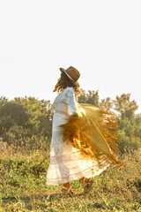 A young woman strolls calmly and casually through a field  she is wearing an open yellow shawl and a brown hat, with her arms spread wide. Boho style. © Светлана 