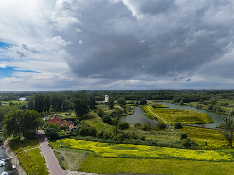 High angle wide horizontal aerial drone photograph of historic white windmill, star fort moat, yellow wildflower field, and village house in Veere, Zeeland, Netherlands on summer day