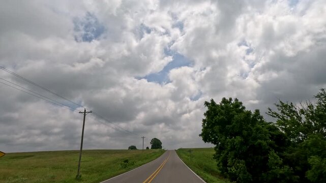 Car POV driving along a country road past rolling green hills with expansive horizon views leading to a farm and red barn in rural Southern Illinois, USA.