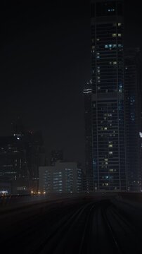 Metro train travels along curving elevated railway tracks through Dubai, passing illuminated skyscrapers at night