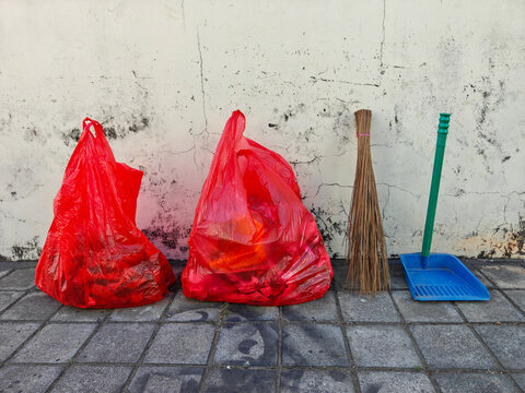 Red Trash Bags, Broom, and Dustpan Standing Against Wall